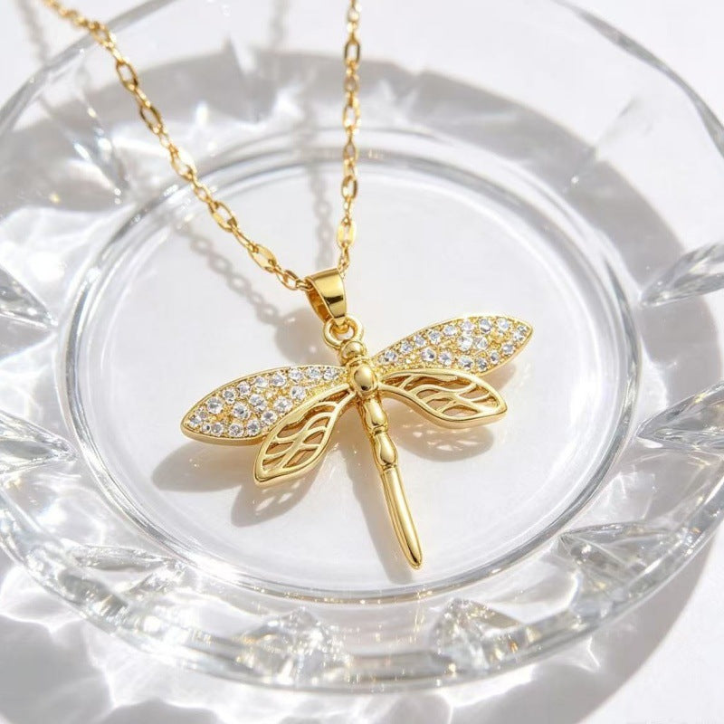 Dragonfly pendant necklace arranged on a clear glass dish, showing the wing details and chain.