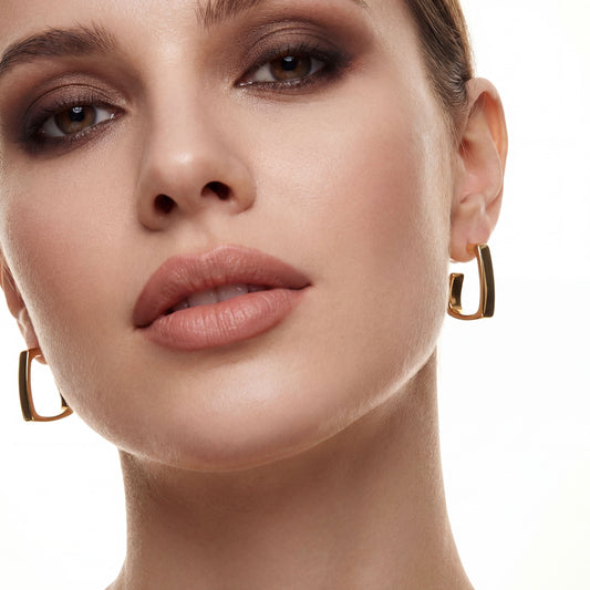 Close-up of a model wearing Ever P. gold tarnish-free geometric hoop earrings. High-end fashion makeup complements the minimalist luxury jewelry design.