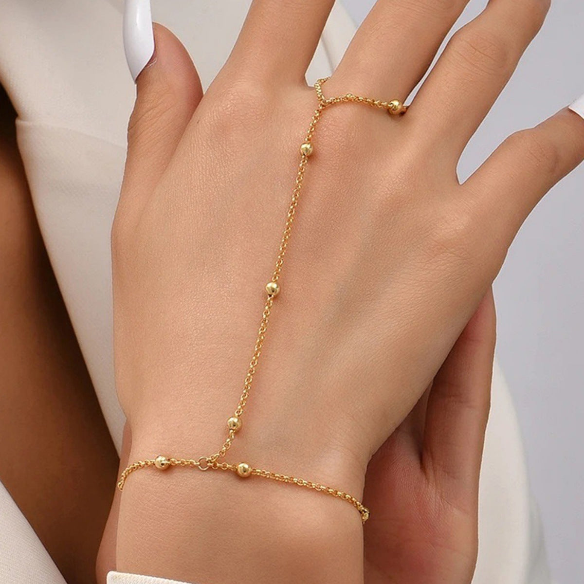 Gold-tone hand chain bracelet with delicate round bead accents draped across the back of a hand and finger.
