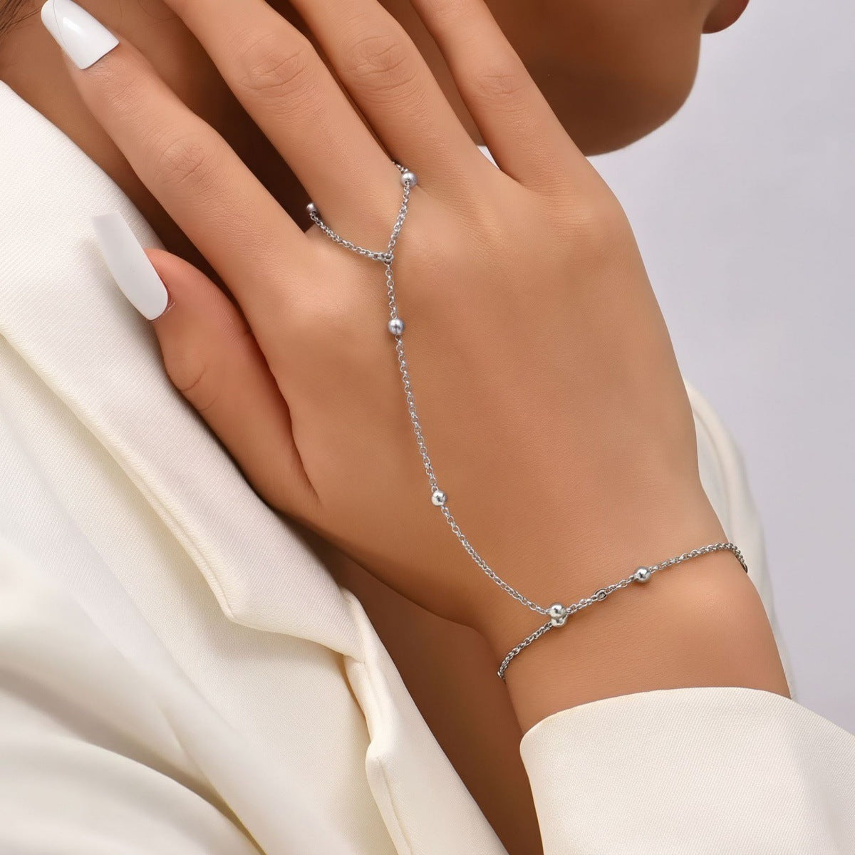Silver-tone finger-to-wrist chain bracelet shown on a hand, highlighting its fine links and scattered round beads.