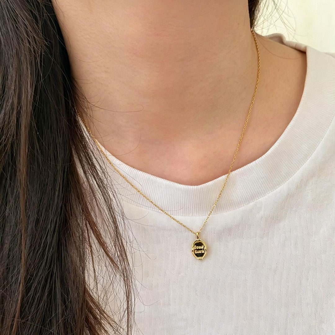Oval Good Luck charm necklace worn over a white crew-neck top, showing how the pendant sits near the neckline.