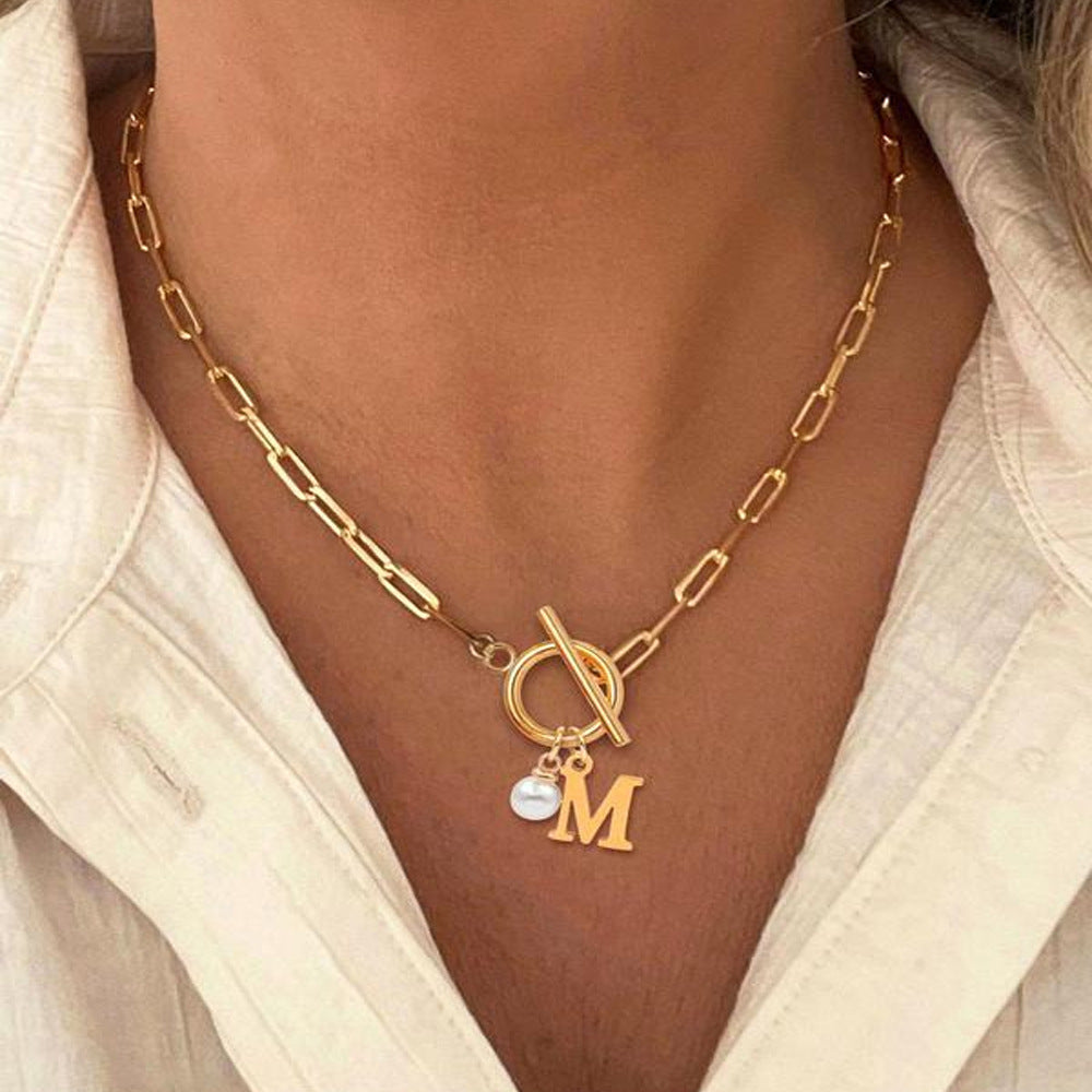 Initial pendant necklace worn at the neckline with a light-colored top, showing its everyday styling.
