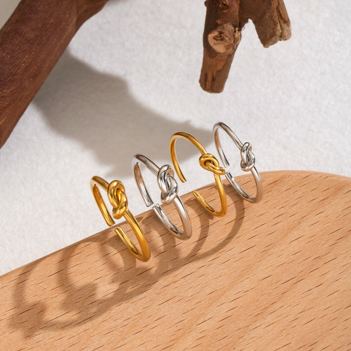 Gold-tone and silver-tone knot rings arranged upright on a wooden surface in warm natural light.