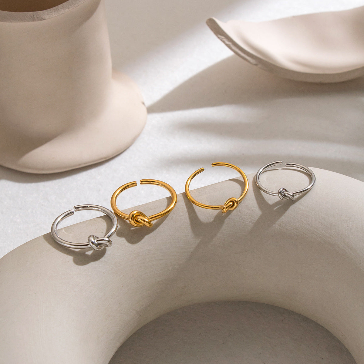 Gold-tone and silver-tone open rings with sculptural knot details arranged on a softly lit neutral display.