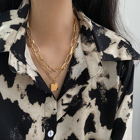 Layered chain necklace with a square pendant styled with a patterned black and cream blouse.