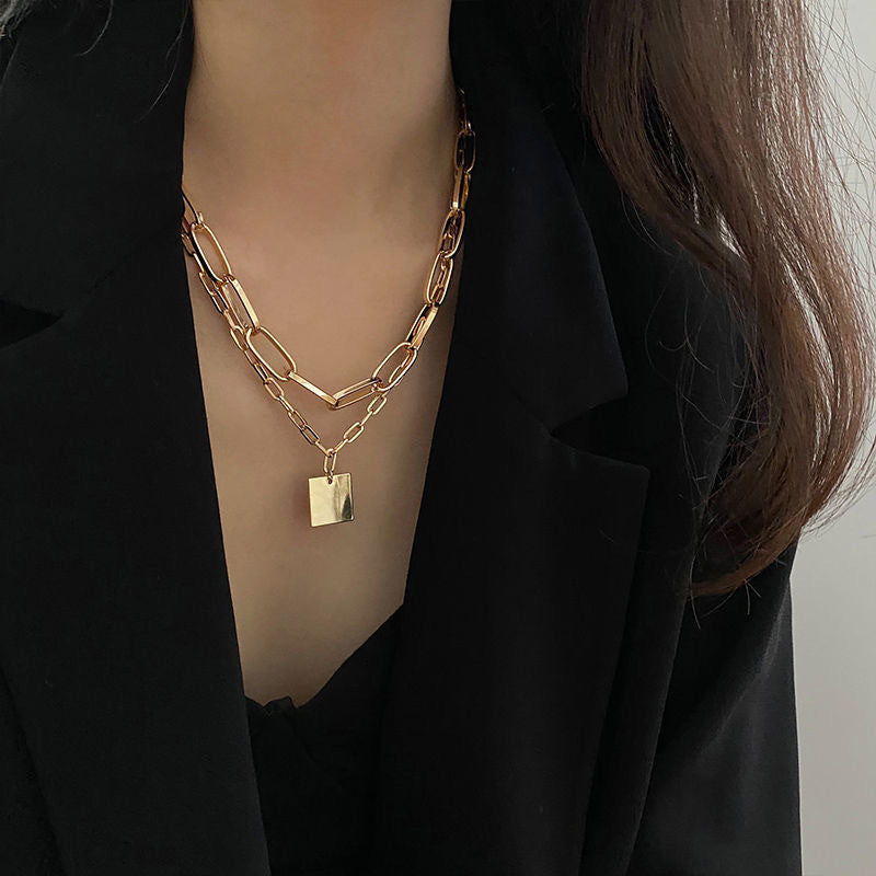 Close-up of a layered necklace with a square pendant worn over a black outfit.