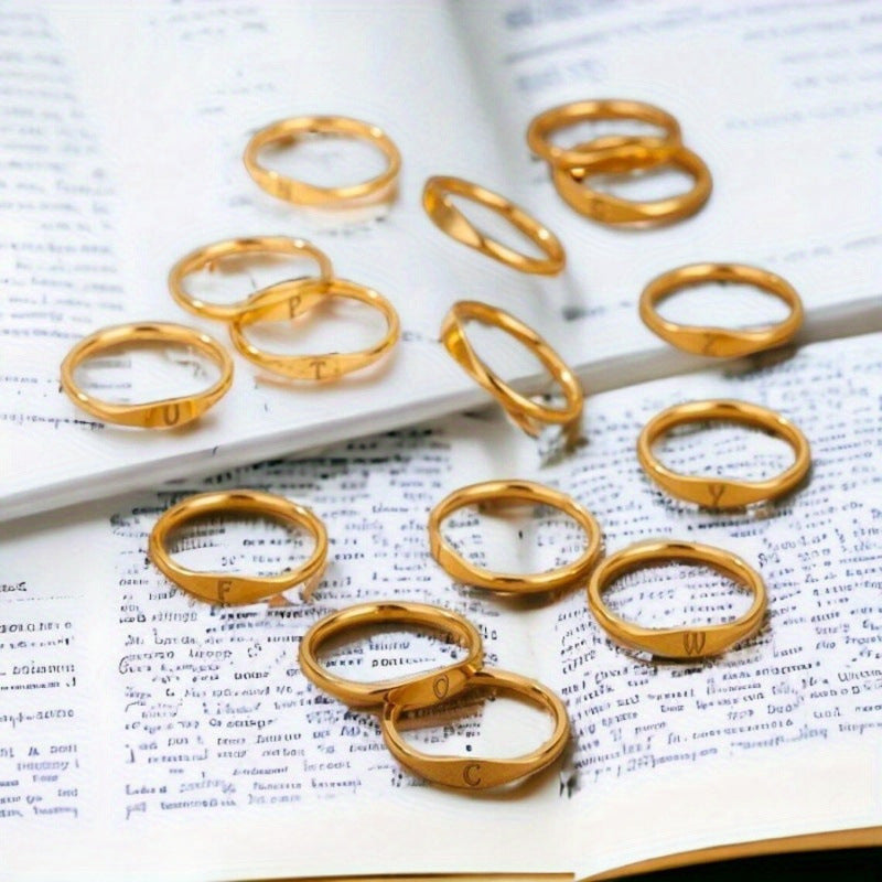 Gold-tone initial rings displayed across an open book, showing different letter designs.