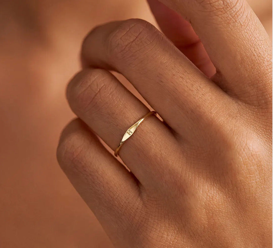 Close-up of a slim initial ring worn on a hand, highlighting its delicate band.