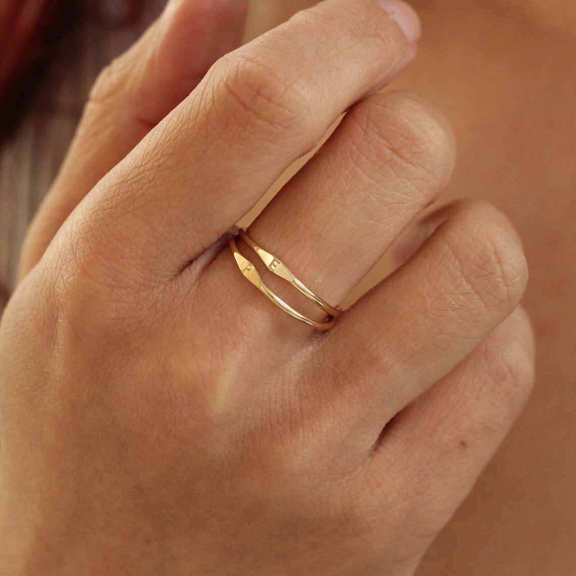 Initial ring worn on a finger, showing the small letter accent from an angled view.