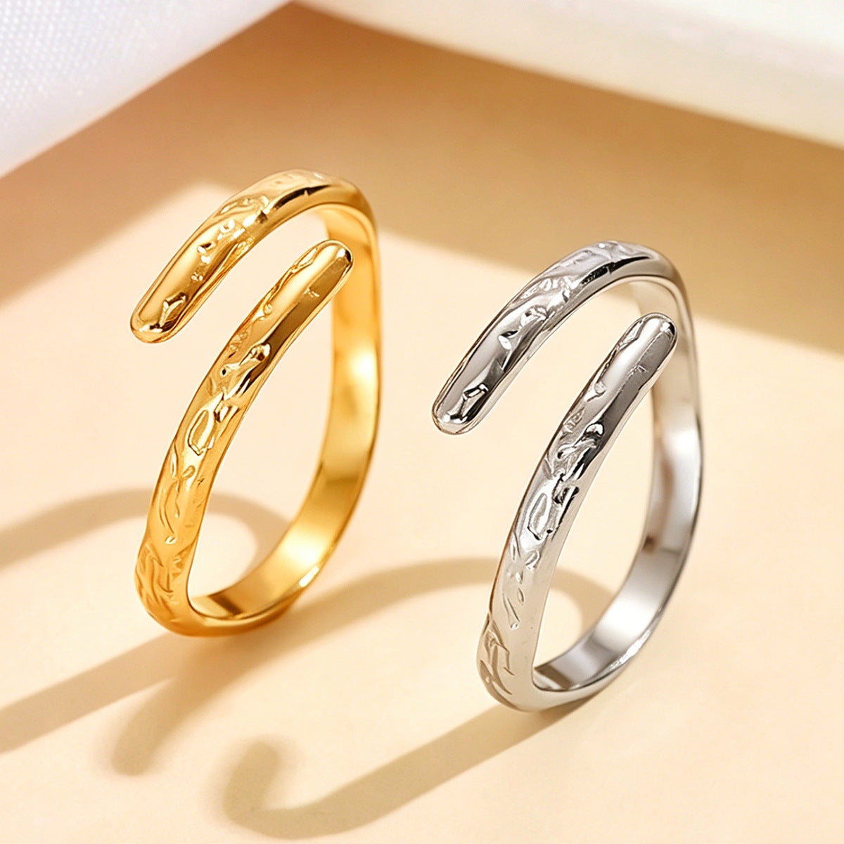 Gold-tone and silver-tone open rings displayed side by side on a beige surface