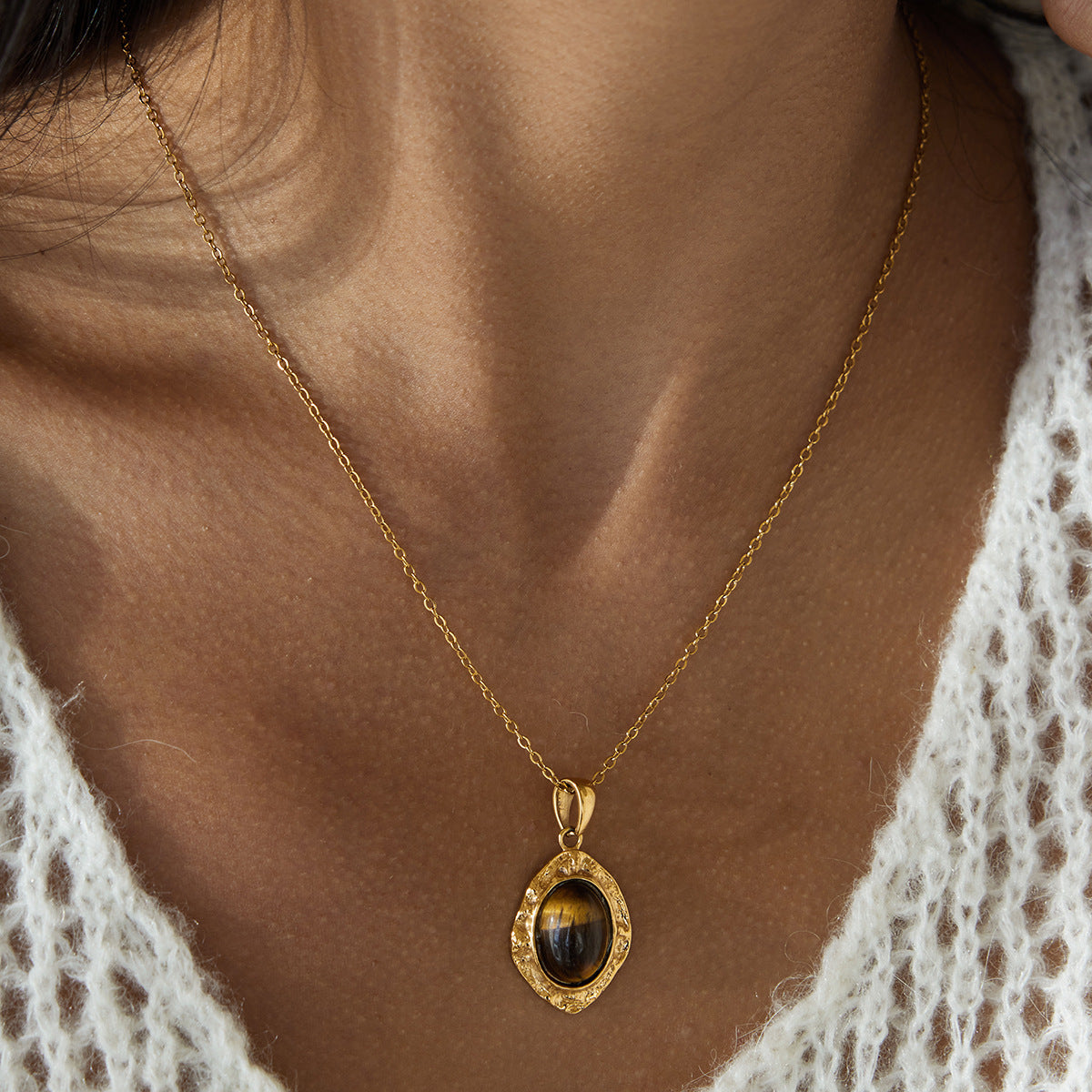 Oval pendant necklace with a brown center worn against a woman's chest with a cream knit top