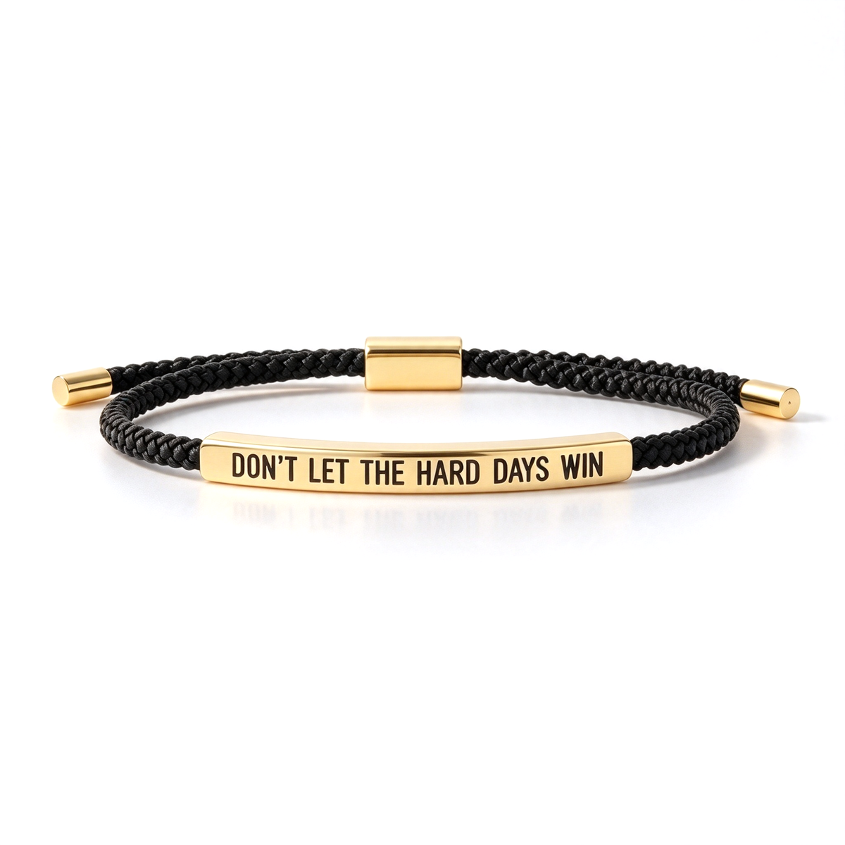 Black braided cord bracelet shown in a low angled view with a silver-tone bar engraved with an encouraging message.