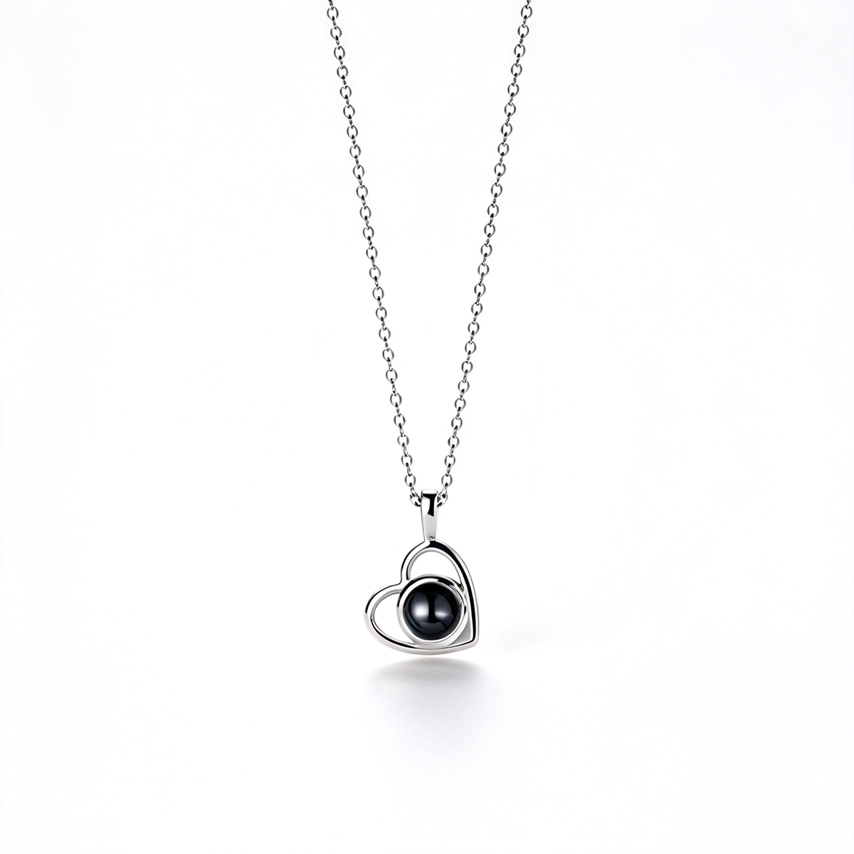 Silver-tone heart pendant with a glossy dark center, shown hanging from a fine chain against a white background.