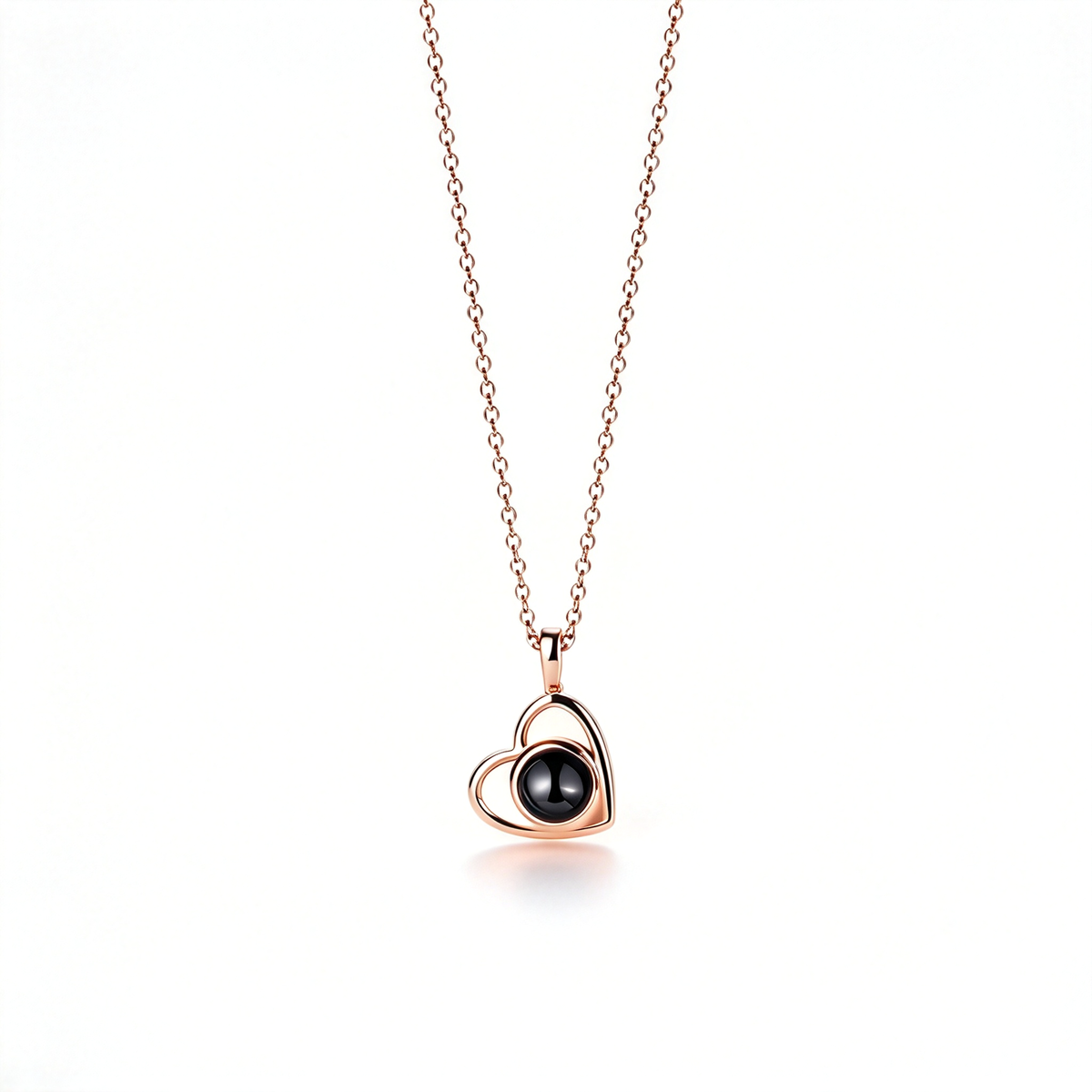 Rose gold-tone heart pendant with a dark round center, displayed vertically on its matching chain against a plain white background.