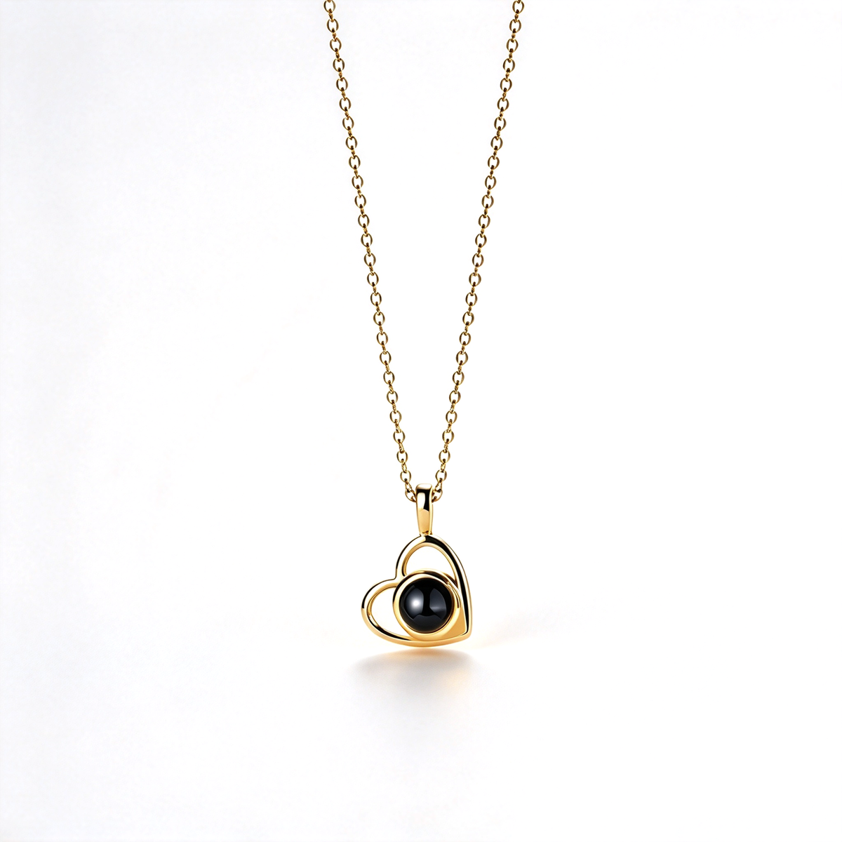 Gold-tone heart pendant with a glossy dark circular center, suspended from a delicate chain in a clean product photograph.