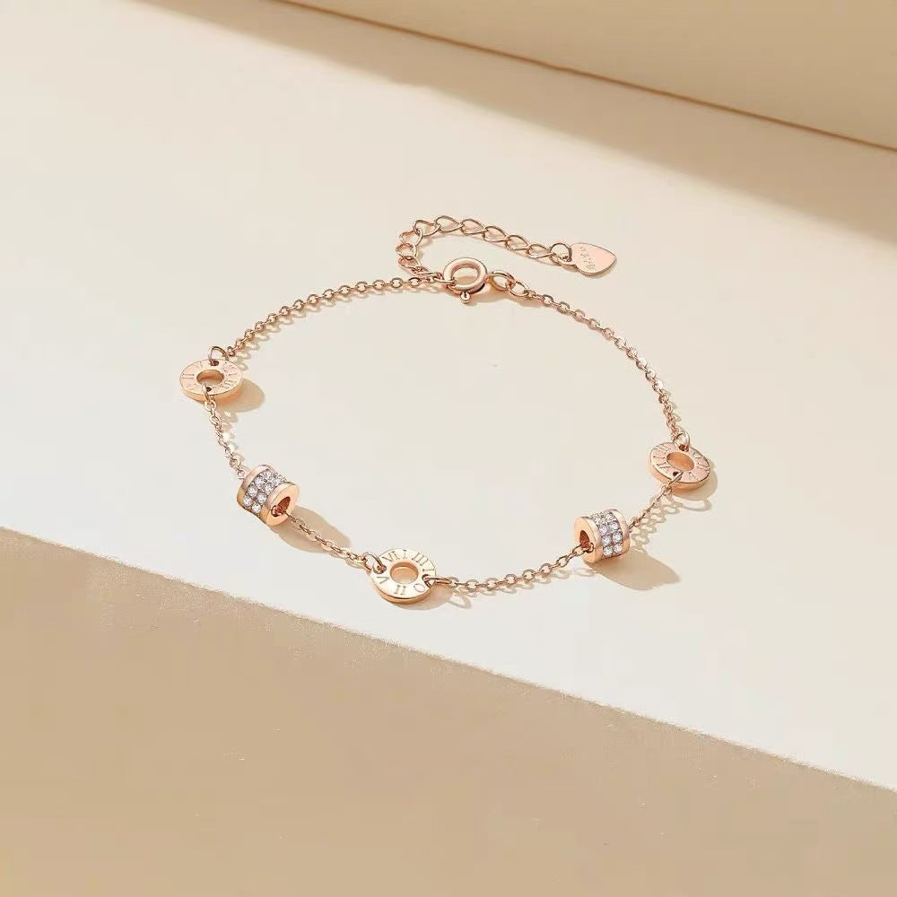 Rose gold-tone charm bracelet arranged on a light surface, showing its circular details and fine chain.