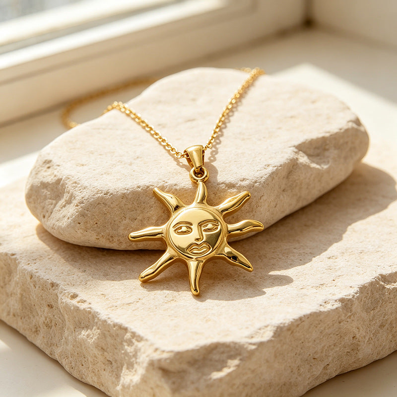 Sun-shaped face pendant and chain arranged on a textured beige stone surface