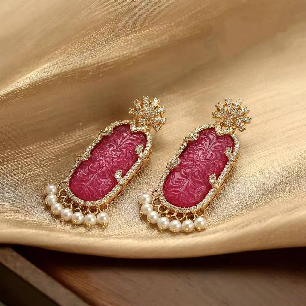 Close-up of the vibrant magenta gemstone earrings with ornate gold carvings.