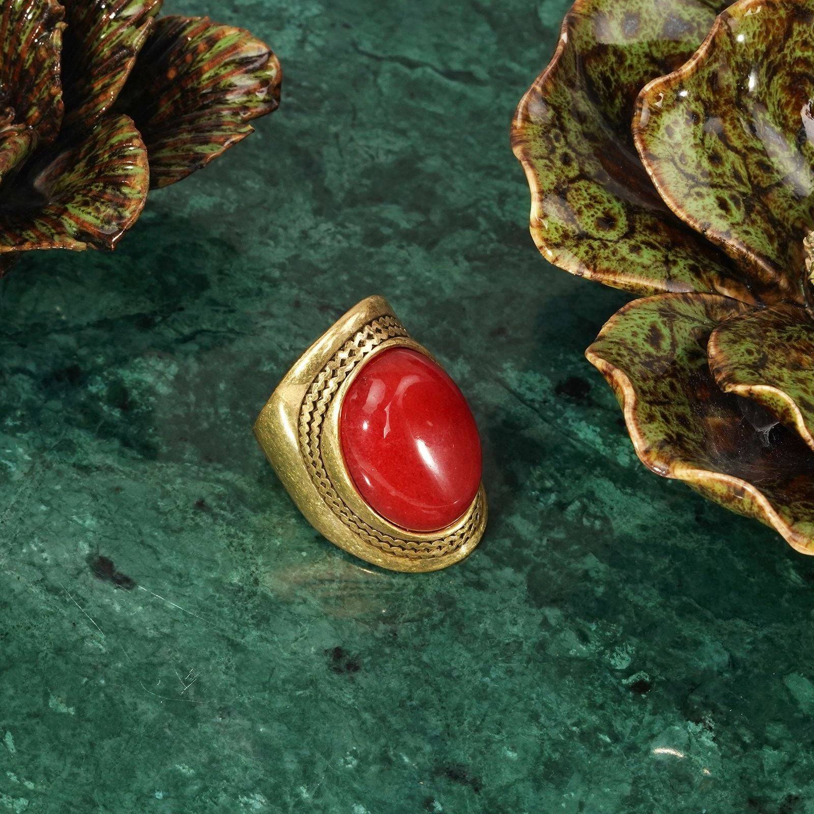 Studio display of the geometric oval cocktail ring with its deep ruby red cabochon and textured royal court details.
