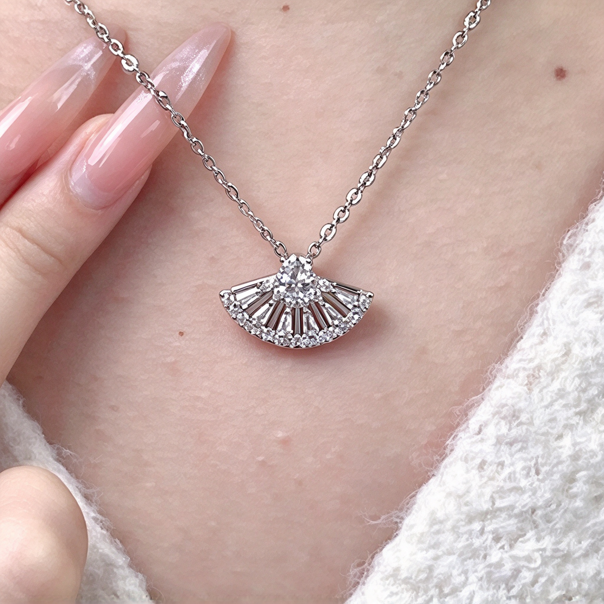 Fan-shaped pendant necklace worn at the neckline, highlighting its delicate chain and sparkling radiating design.