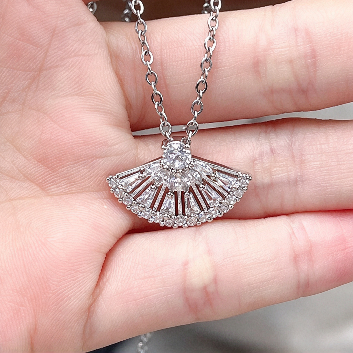 Close-up of the fan-shaped pendant held against an open palm, showing its radiating decorative pattern.
