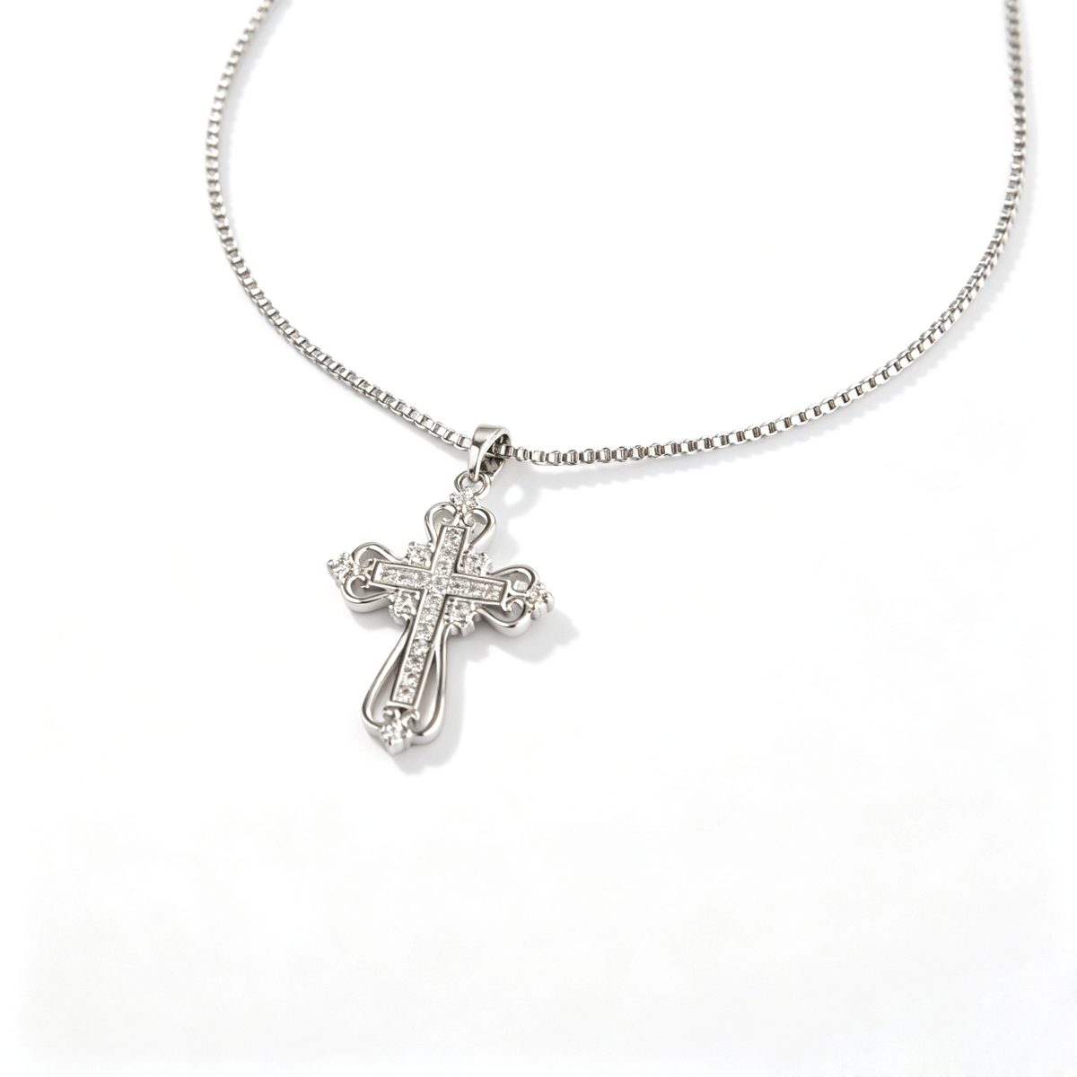 Angled close-up of an intricate scrollwork filigree cross pendant with clear pave stones.