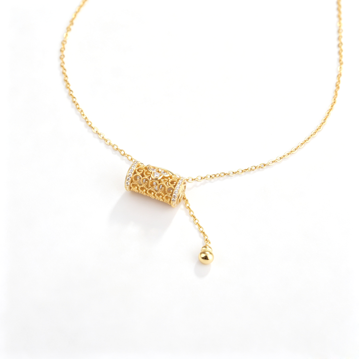 Angled close-up of a gold-tone filigree barrel lock pendant with sparkling accents and bead tassel.