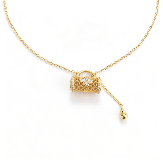 Front close-up of a gold-plated filigree lock pendant with floral pavé center and drop tassel.