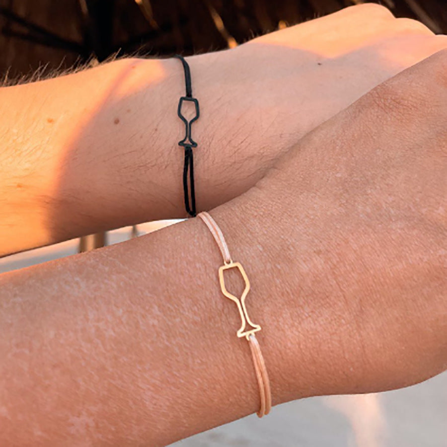A close-up of a wrist wearing a delicate fish charm cord bracelet with a gold-tone outline charm.