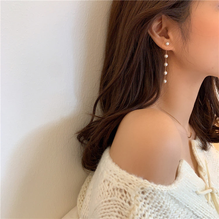 Side view of a woman wearing a long five-pearl drop earring with her hair tucked behind her ear