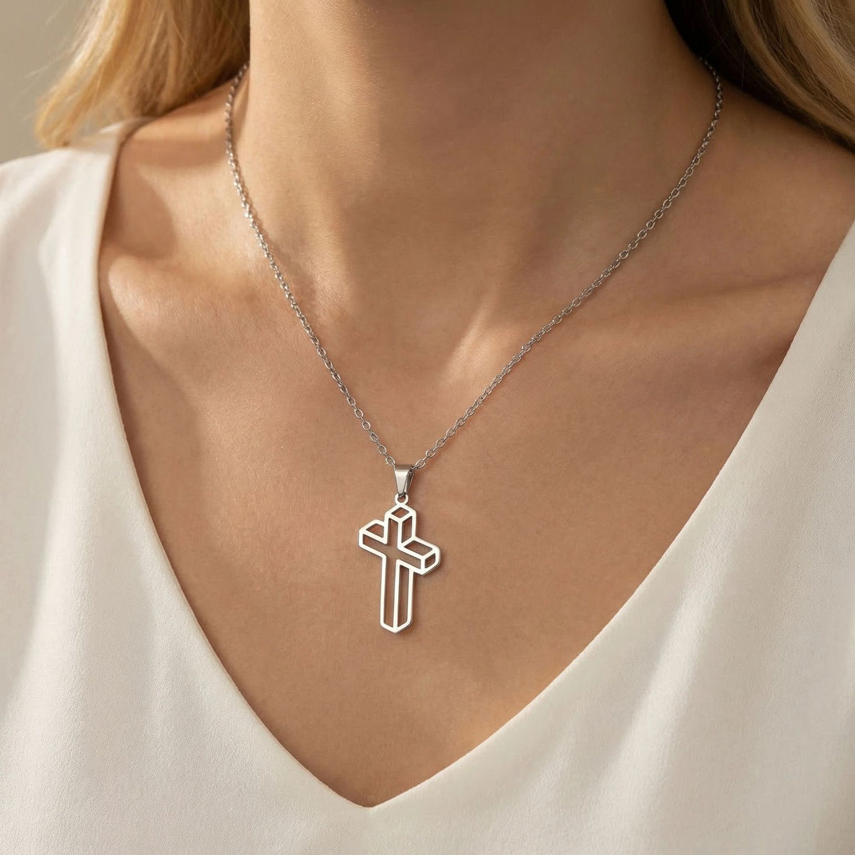 Silver-tone geometric cross pendant necklace worn with a white V-neck top.
