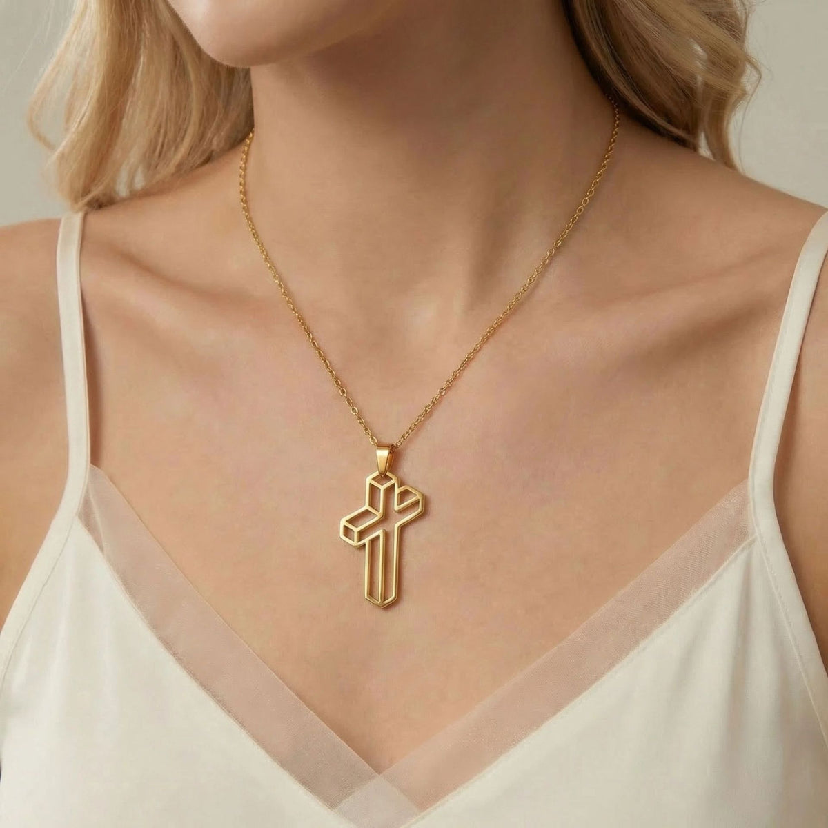 Gold-tone geometric cross pendant necklace styled with a cream camisole.