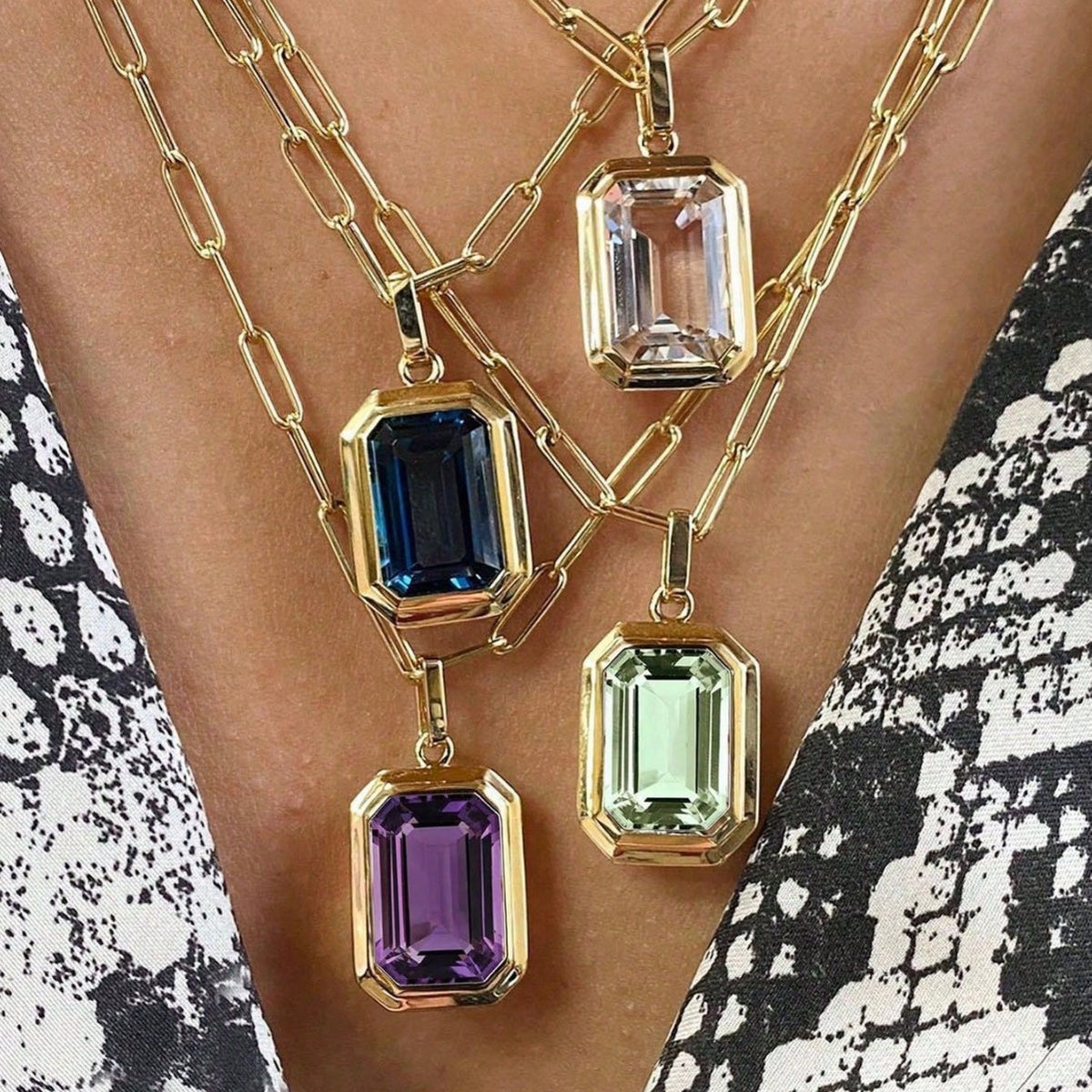 Four geometric pendant necklaces in blue, green, purple, and clear displayed together.