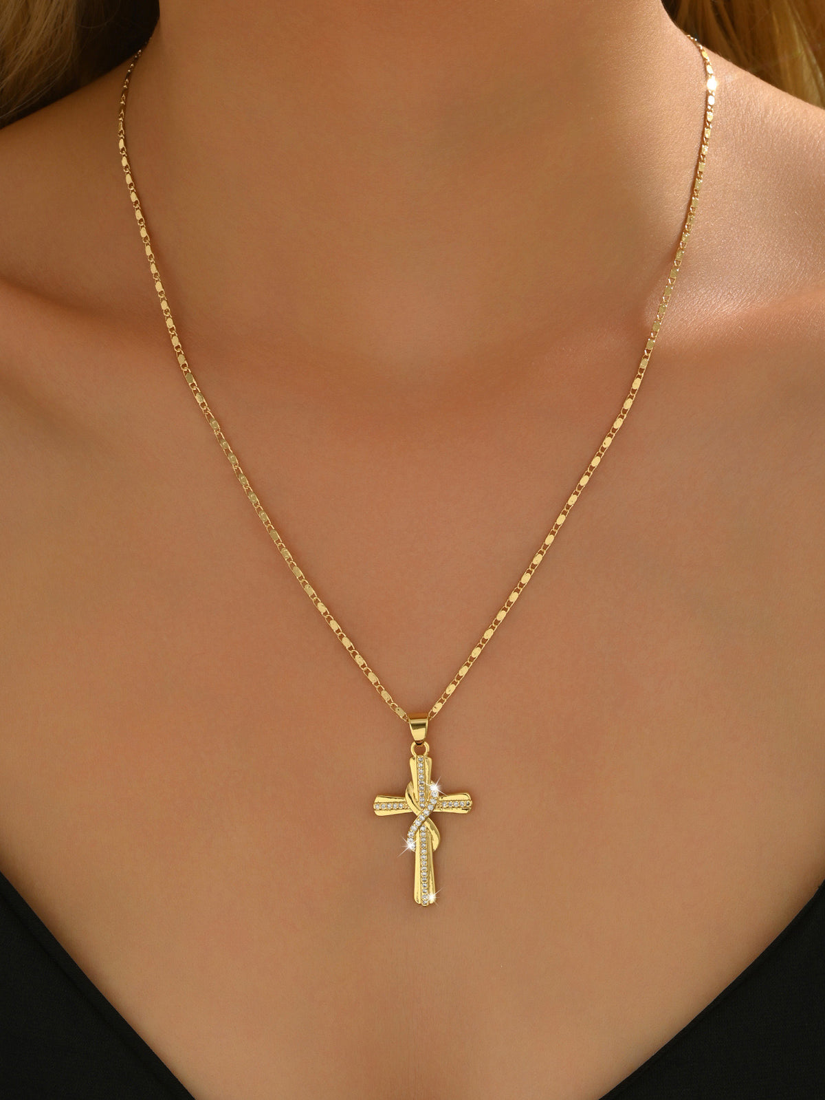 Gold cross pendant necklace worn on the chest with a simple V-neck top