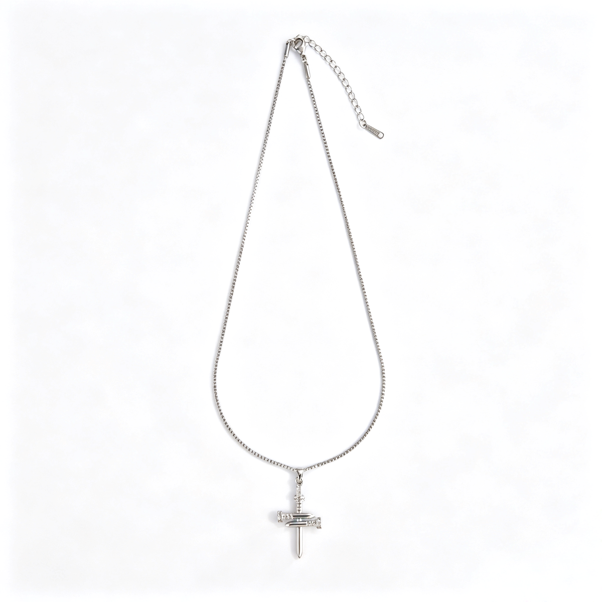 Angled close-up of industrial nail cross pendant showing glossy silver finish