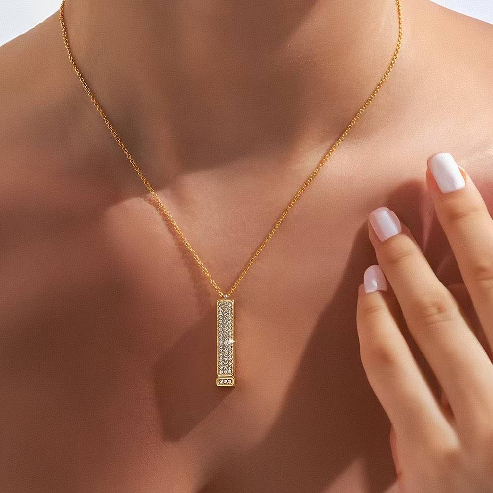 Gold-tone bar pendant necklace worn at the center of the chest