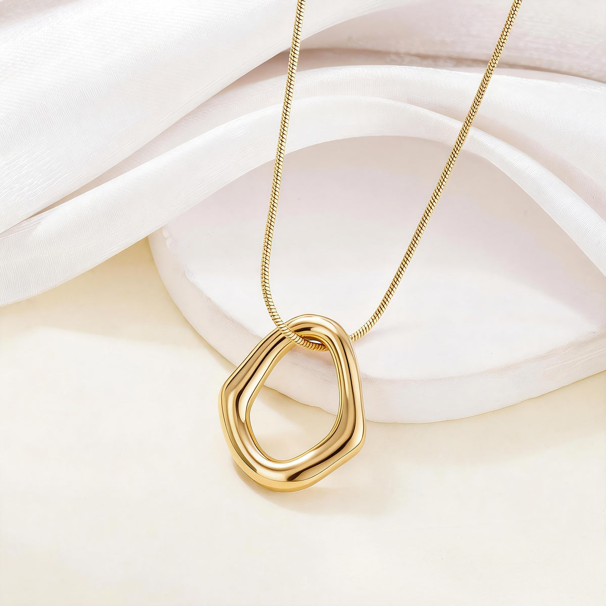 Gold-tone geometric pendant necklace styled on a soft ivory fabric backdrop.