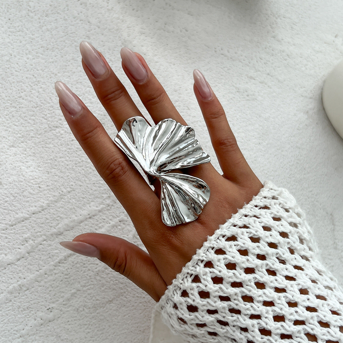 Model hands wearing both gold and silver versions of the 3D ginkgo leaf ring against knitwear.