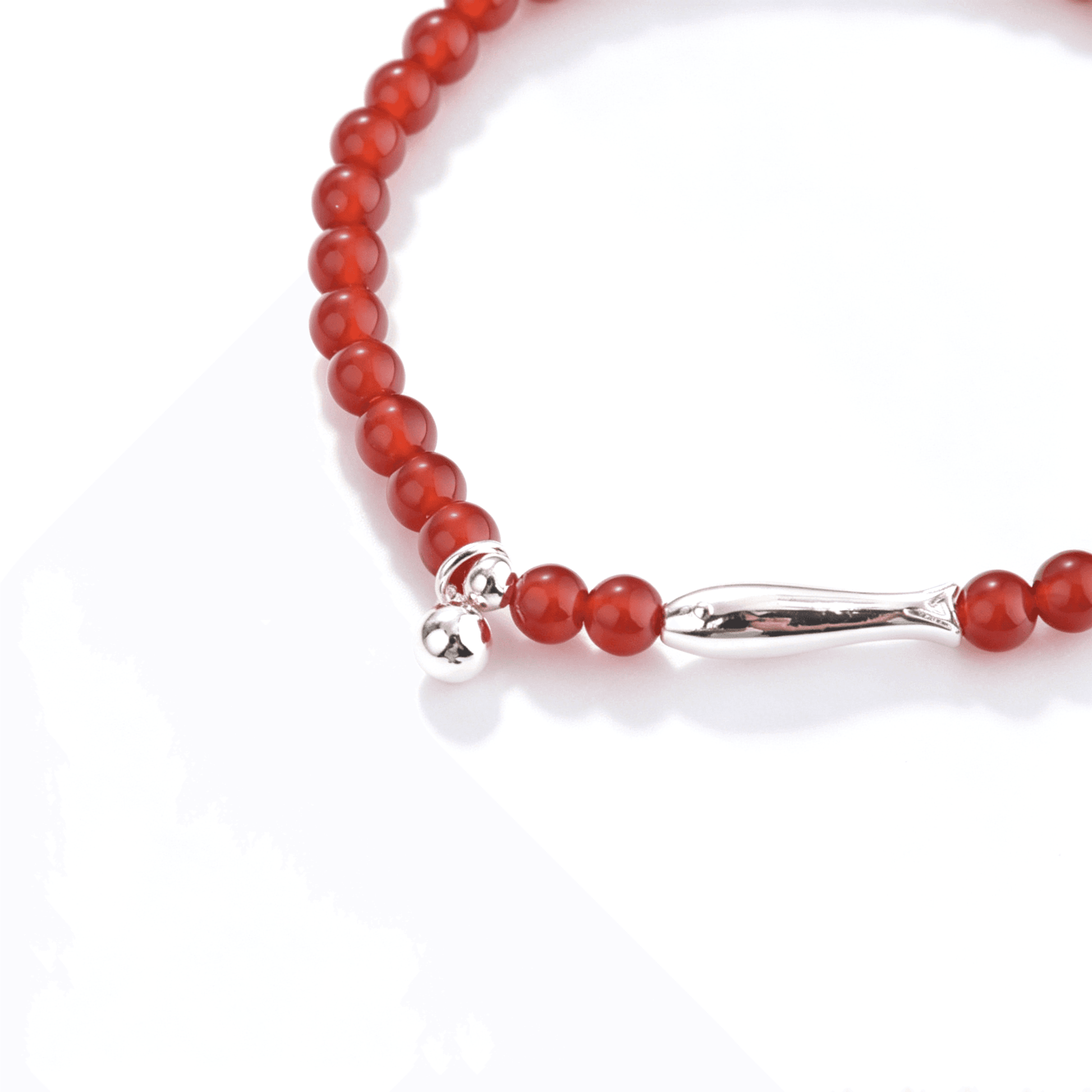 Close-up of the silver-tone koi centerpiece and spherical charm on a translucent red agate bracelet.