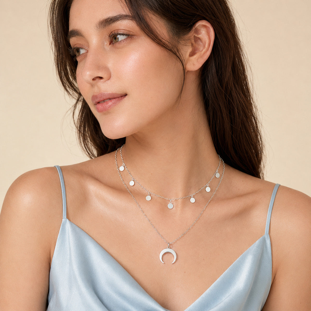 Layered crescent moon necklace styled with a round charm chain over a light blue camisole.