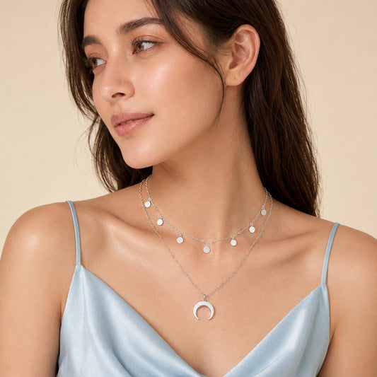 Layered crescent moon necklace styled with a round charm chain over a light blue camisole.