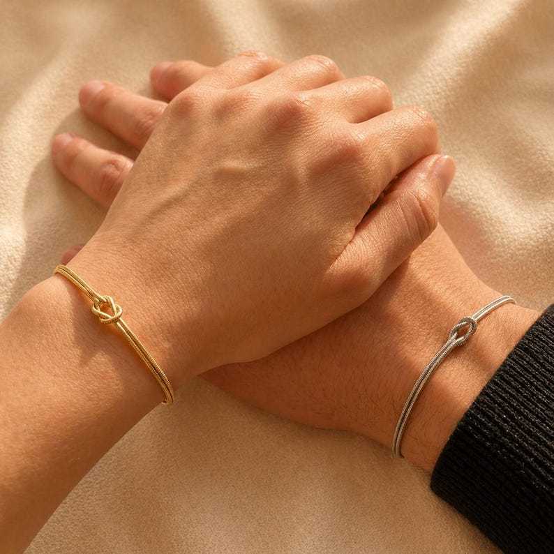 Two people wearing matching gold-tone and silver-tone knot bracelets while holding hands.