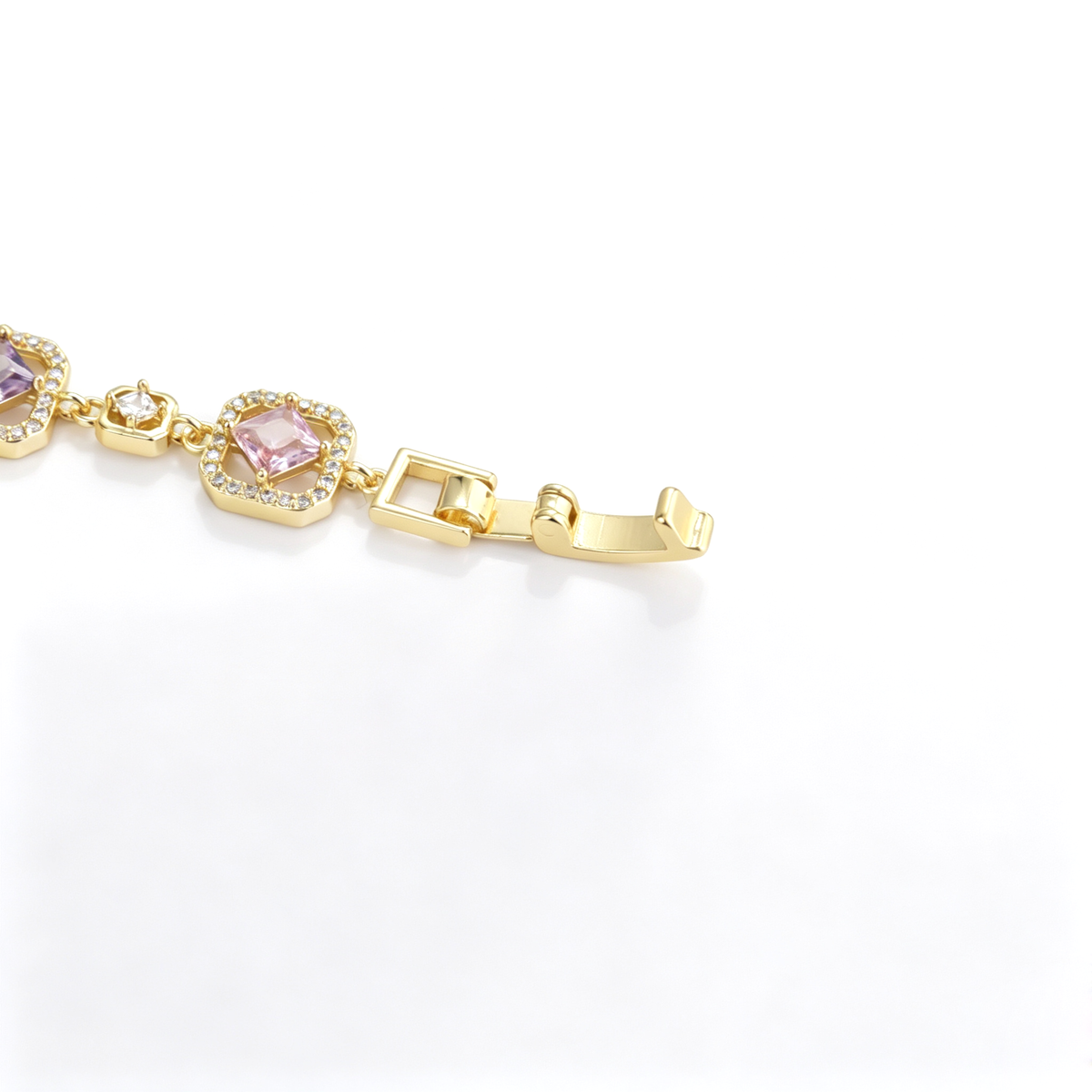 Open fold-over clasp mechanism on a gold-tone station bracelet with pink cubic zirconia accents.