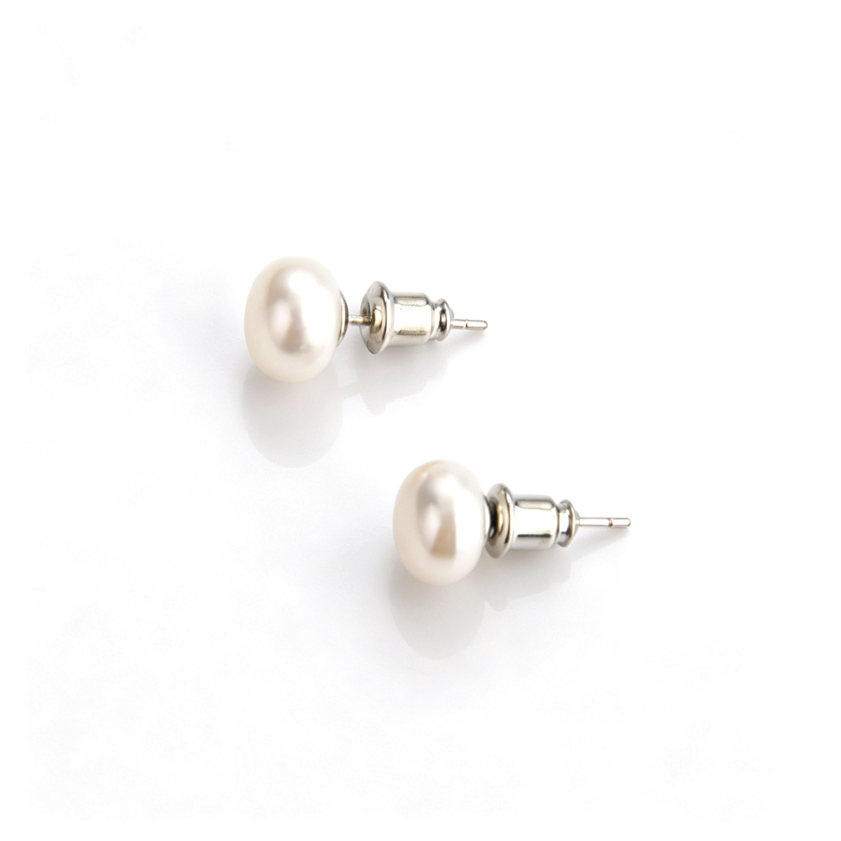 Angled view of shiny natural white pearl stud earrings resting on a smooth reflective background.