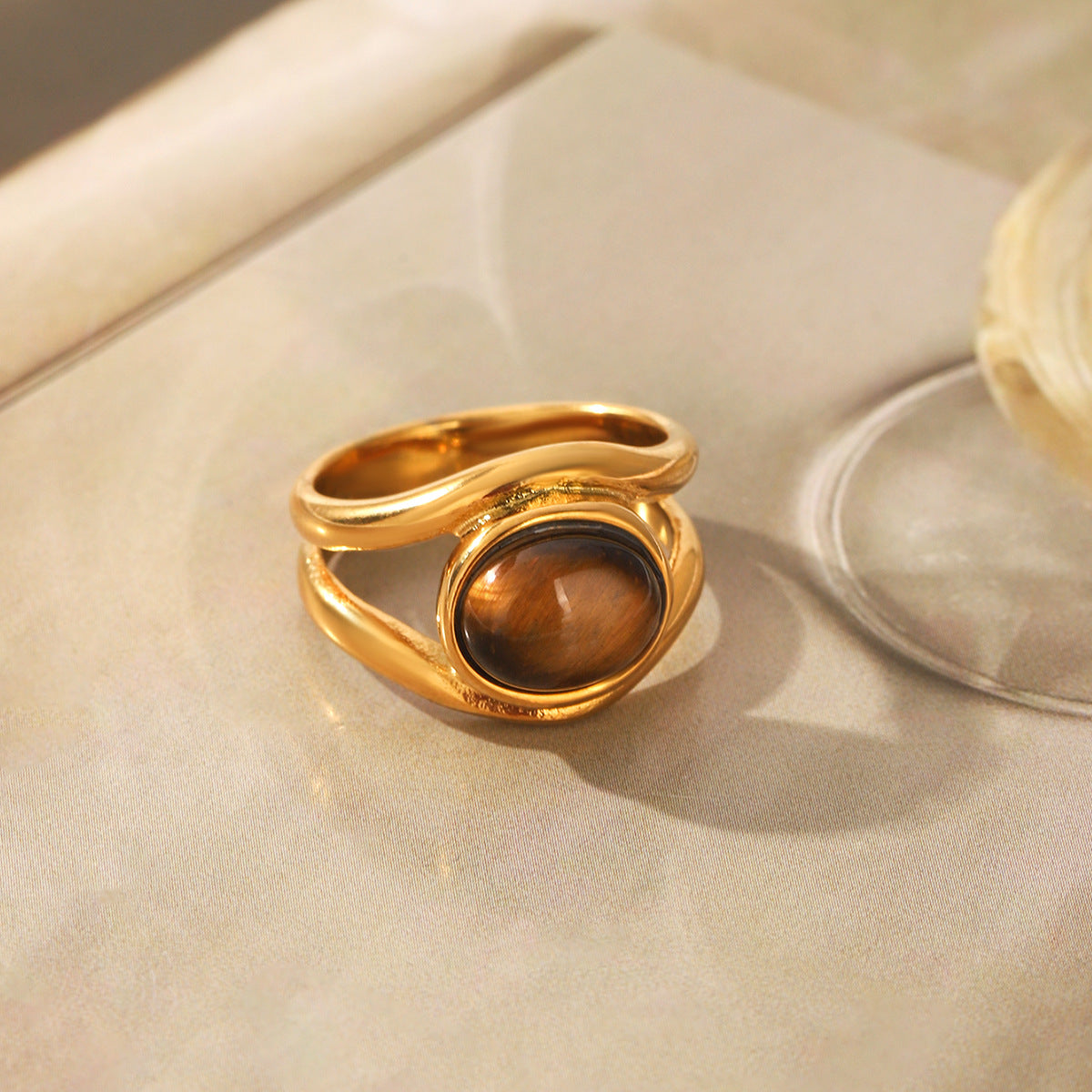 The oval centerpiece ring displayed on a pale surface beside soft neutral styling props.