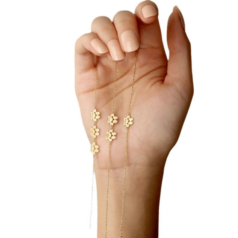 Gold-tone paw charm bracelet displayed across an open palm to show the charm design.