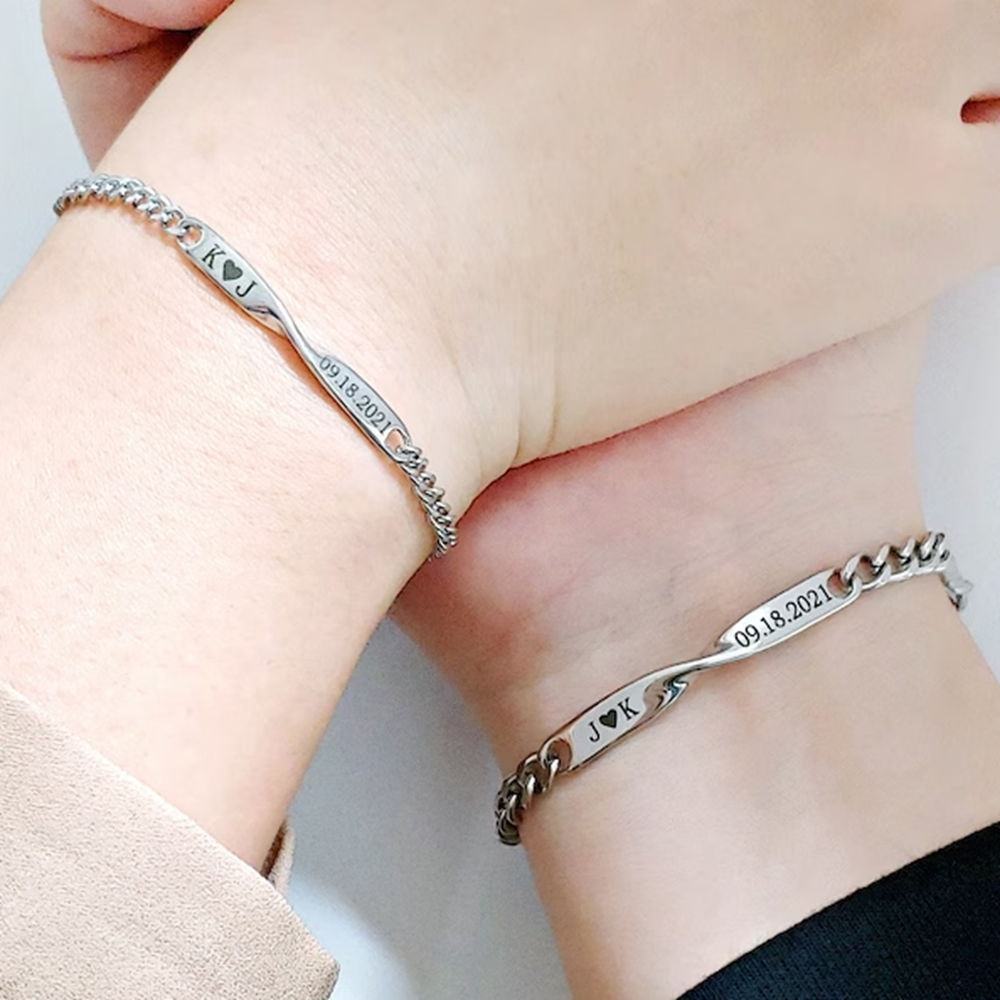 Two matching chain bracelets worn on separate wrists, displaying personalized nameplates and engraved dates