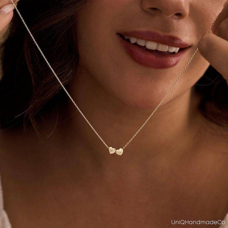 Woman holding a dainty gold-tone engraved heart necklace below her chin. | 