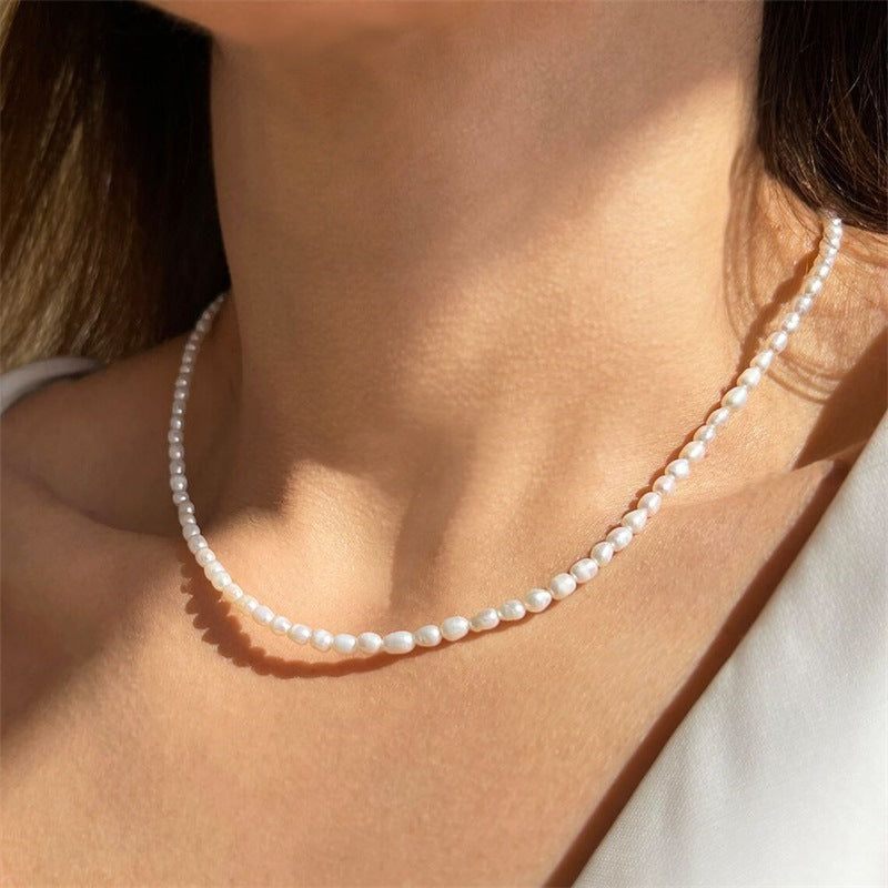 Close-up of a woman wearing a delicate beaded necklace with a fine, rounded design against her neckline.