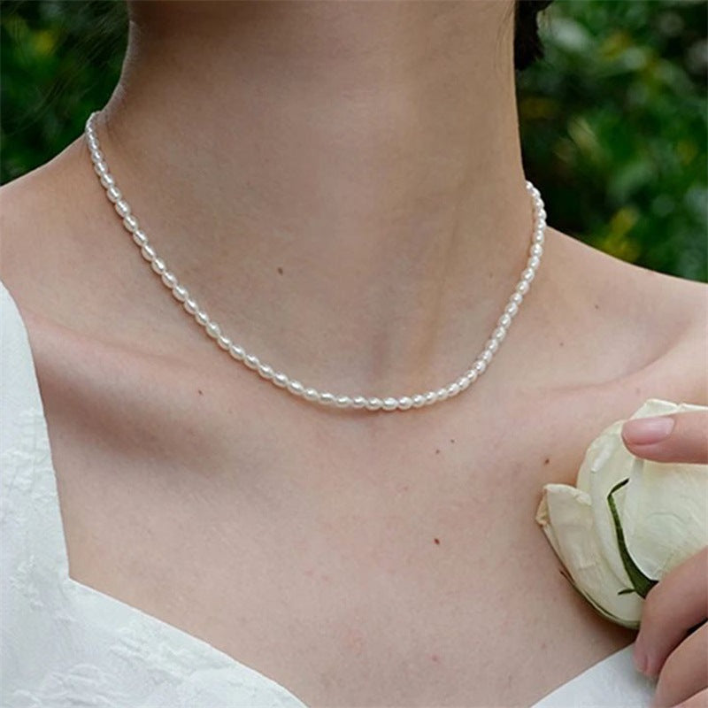 Woman wearing a petite beaded necklace with a white dress and holding a white rose outdoors.